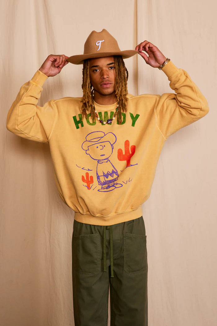 Person wearing yellow sweatshirt features Peanuts character, Charlie Brown, who is charmingly reinterpreted as a laid-back cowboy.