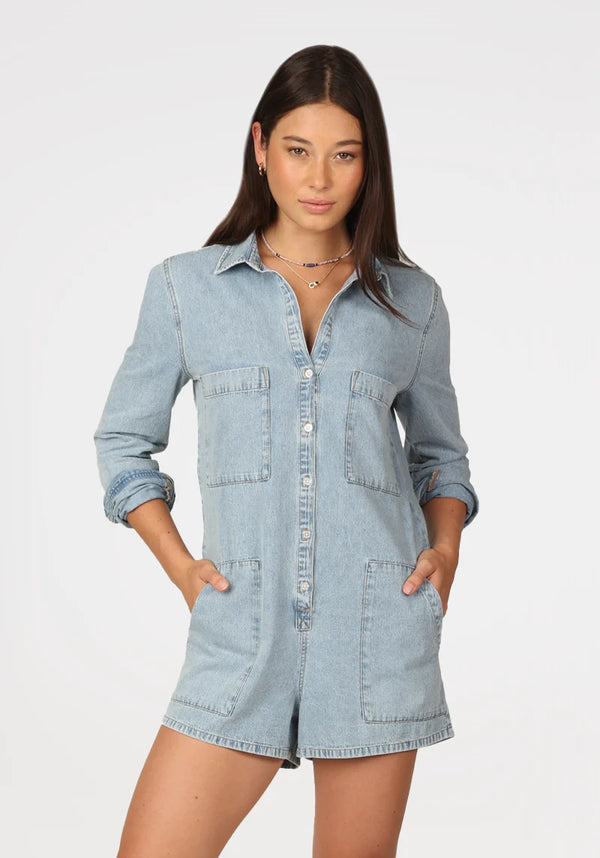 Woman wearing denim long sleeve romper with button front and functional pockets on side and breast