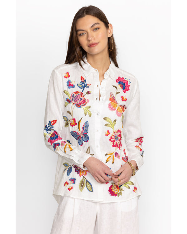 Woman wearing white button down linen blouse with multicolor flowers and butterflies embroidered throughout
