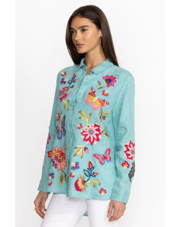 Woman wearing bright blue button up blouse with multicolor flowers and butterflies embroidered throughout 