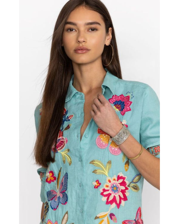 Woman wearing bright blue button up blouse with multicolor flowers and butterflies embroidered throughout