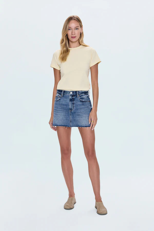Woman wearing a yellow t-shirt and denim skirt on a light blue background