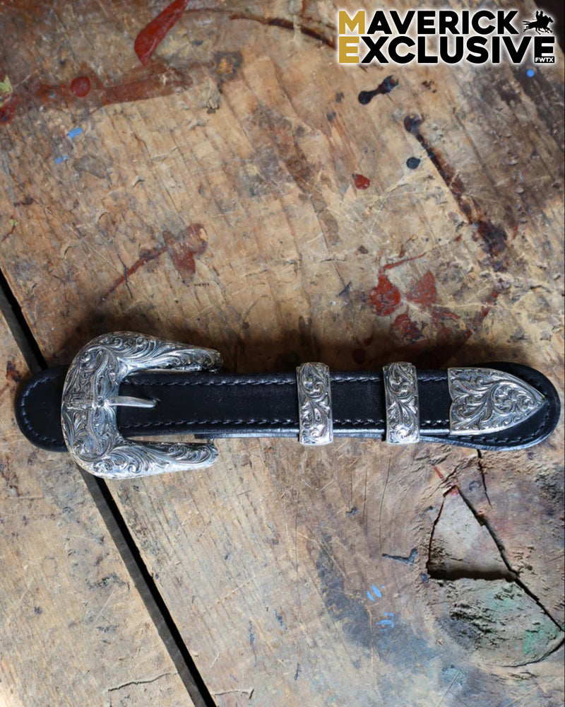 Black leather belt with silver buckle on a rustic wooden surface, featuring 'Maverick Exclusive' branding.