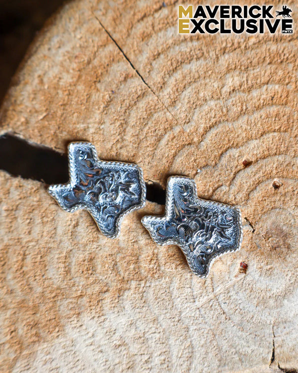 Silver Texas-shaped earrings on a wooden surface with 'Maverick Exclusive' branding.