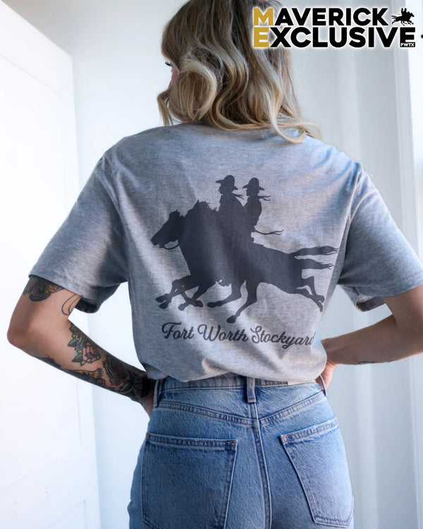 Person wearing a gray t-shirt with horse and rider design and 'Fort Worth Stockyard' text, standing against a white curtain.