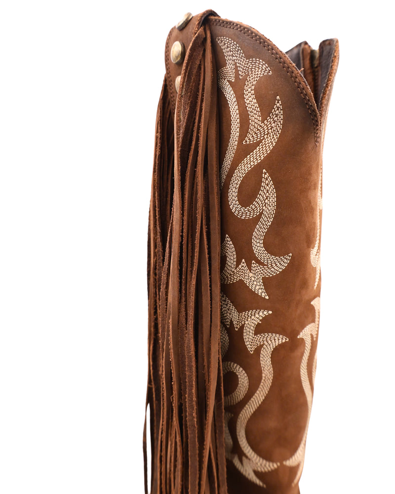 Tall brown boot with white western embroidery with long fringe on the outsides on the boot with brass studs going down the boot. The inside of the boot has a zipper