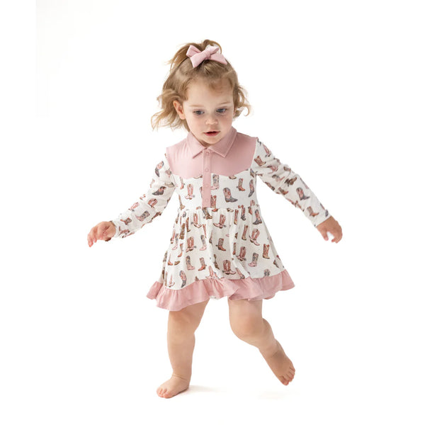 Child wearing a pink dress with cowboy boot pattern on a white background