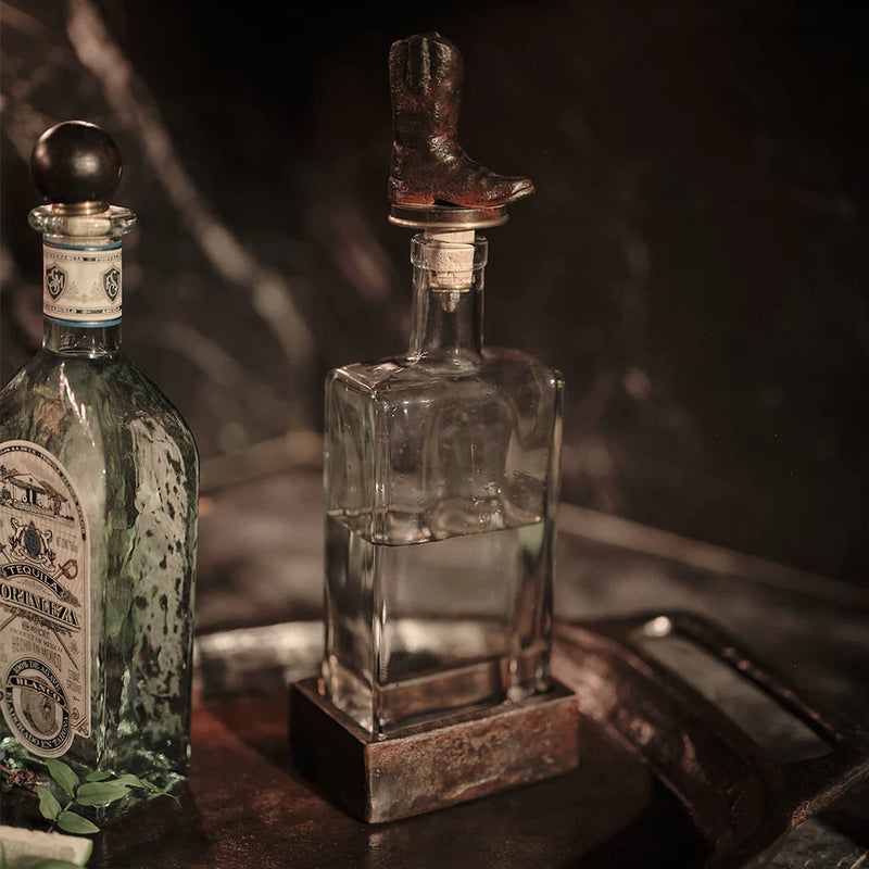 Two bottles, one with a label and the other with a cowboy boot on top, against a dark background.