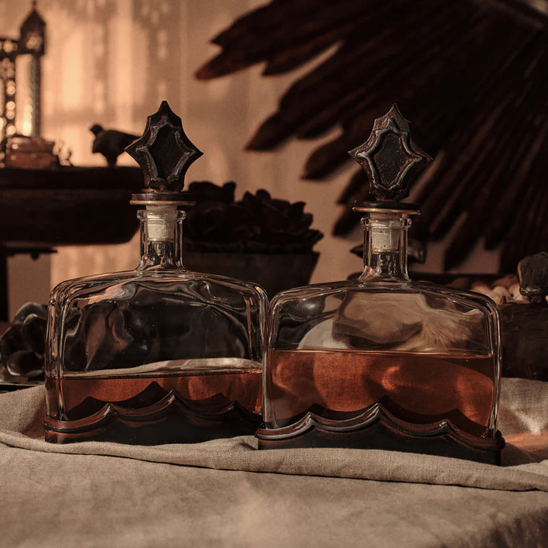 Two glass decanters with star-shaped stoppers on a textured surface.