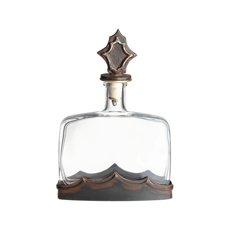 Clear glass decanter with decorative metal cap on a white background