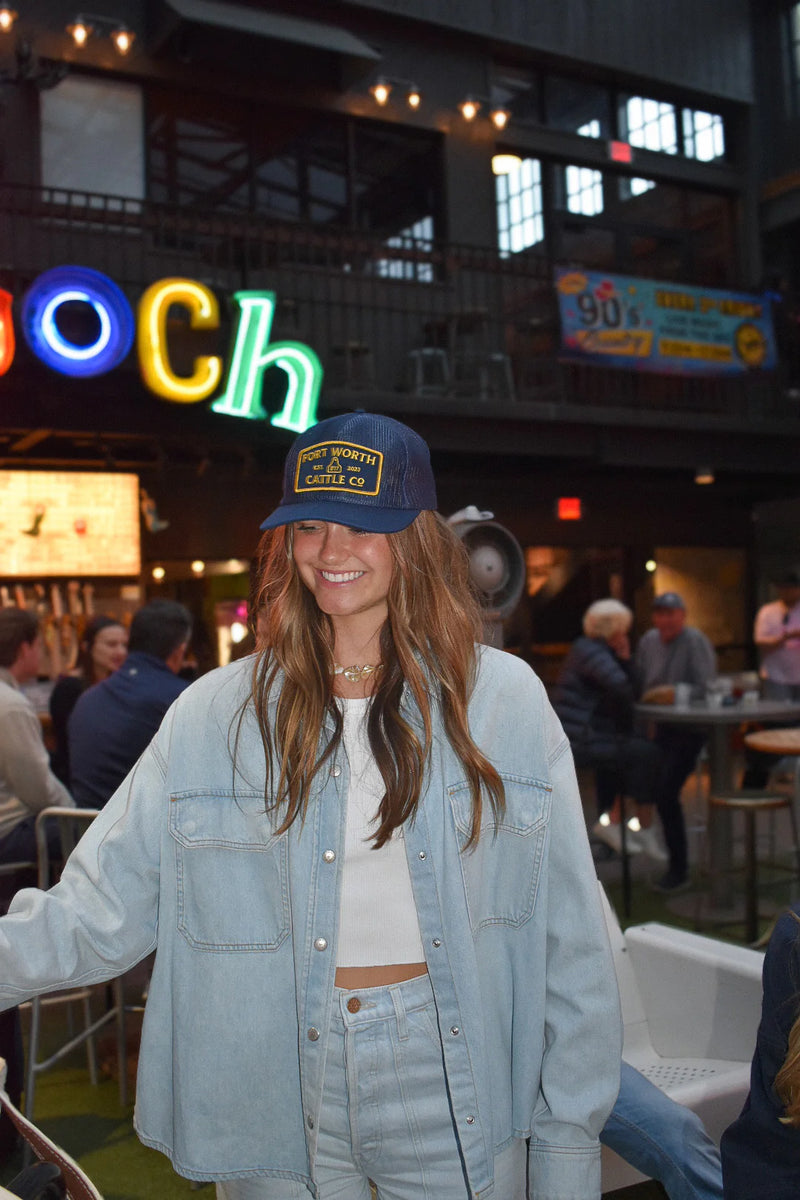 Woman wearing a blue cap and light blue jacket in a casual indoor setting with neon signs.
