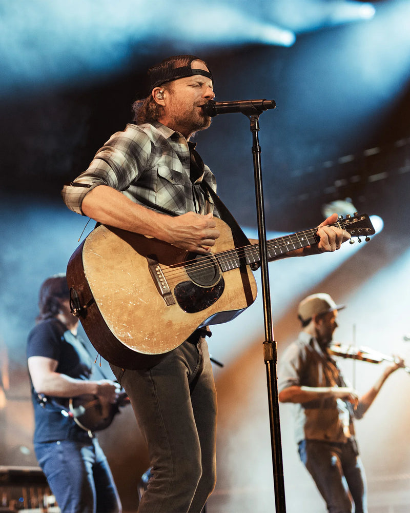 Man playing guitar on stage with a microphone, surrounded by other musicians.