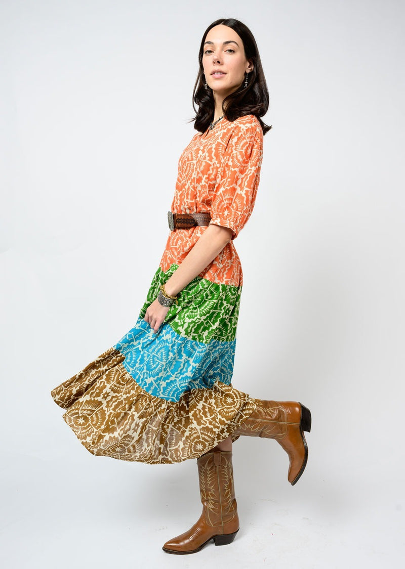 Woman wearing a colorful dress with a patterned skirt and brown boots on a white background
