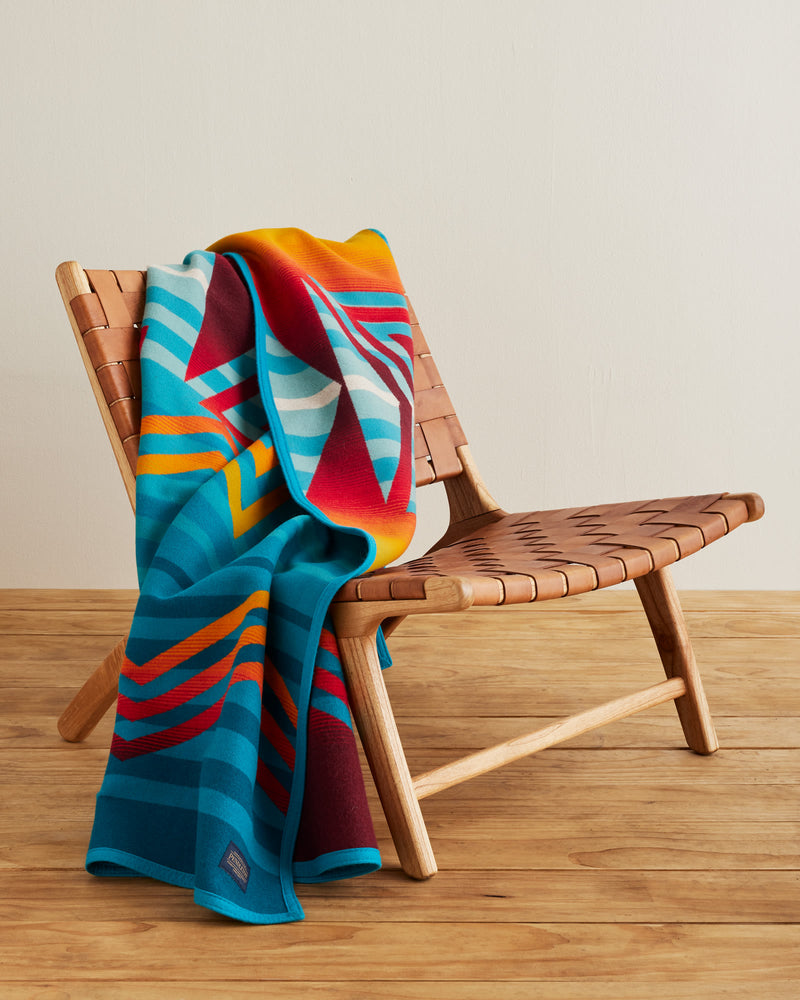 BLUE STRIPE PATTERN BLANKET WITH RED, YELLOW AND ORANGE ZIG ZAG PATTERN OVER IT