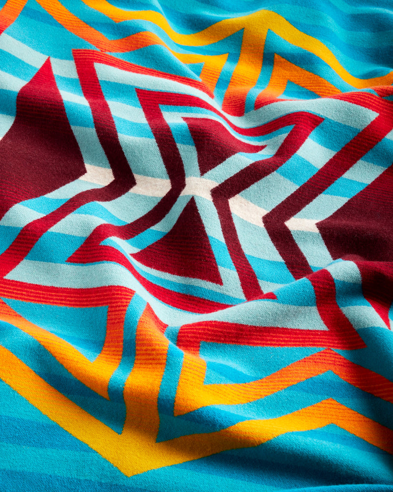 BLUE STRIPE PATTERN BLANKET WITH RED, YELLOW AND ORANGE ZIG ZAG PATTERN OVER IT