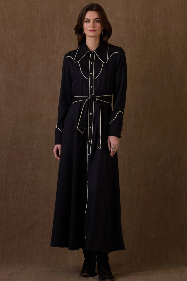 Woman wearing a black dress with white trim against a brown background