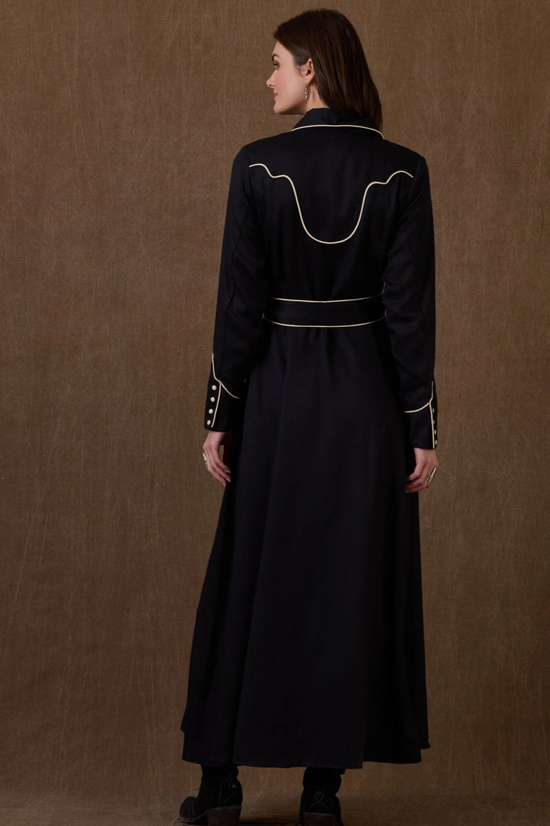 Woman wearing a black dress with white embroidery against a brown background