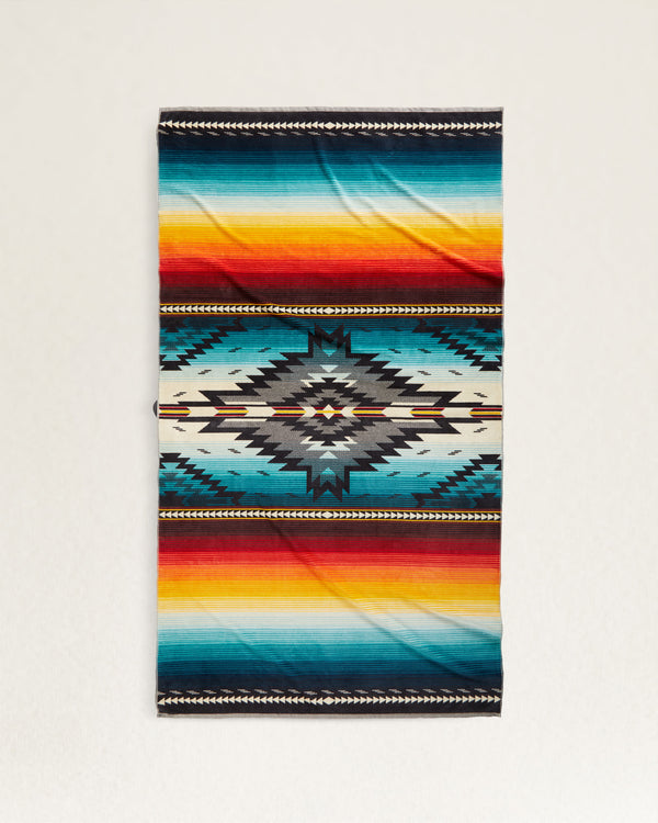 Oversized towel with aztec print in the center fading into serape design. Colors include red, orange, yellow, blue and black