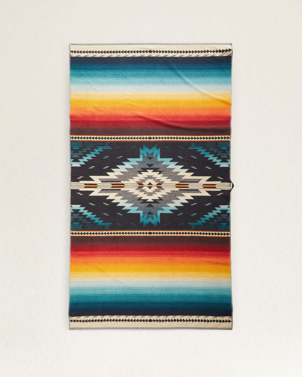 Oversized towel with aztec print in the center fading into serape design. Colors include red, orange, yellow, blue and black.