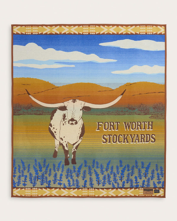 Decorative blanket with a longhorn cow and 'Fort Worth Stockyards' text on a scenic background.