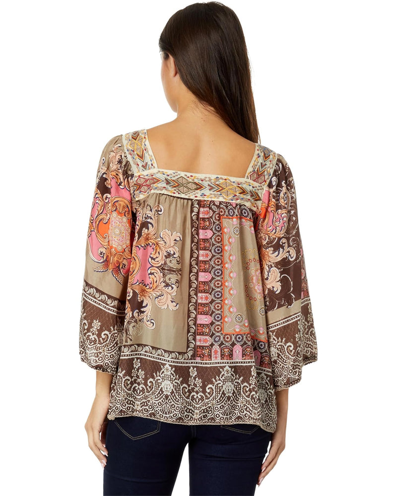 Woman wearing square neckline blouse with ornate warm toned color pattern.