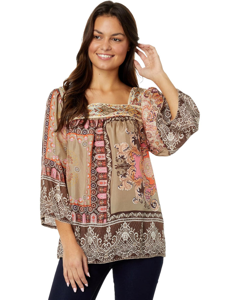 Woman wearing square neckline blouse with ornate warm toned color pattern.