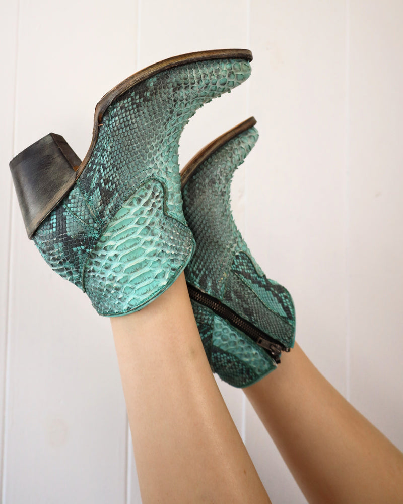 A lady with her feet up wearing CORRAL WOMEN'S FULL PYTHON TURQUOISE ROUND TOE BOOTIES