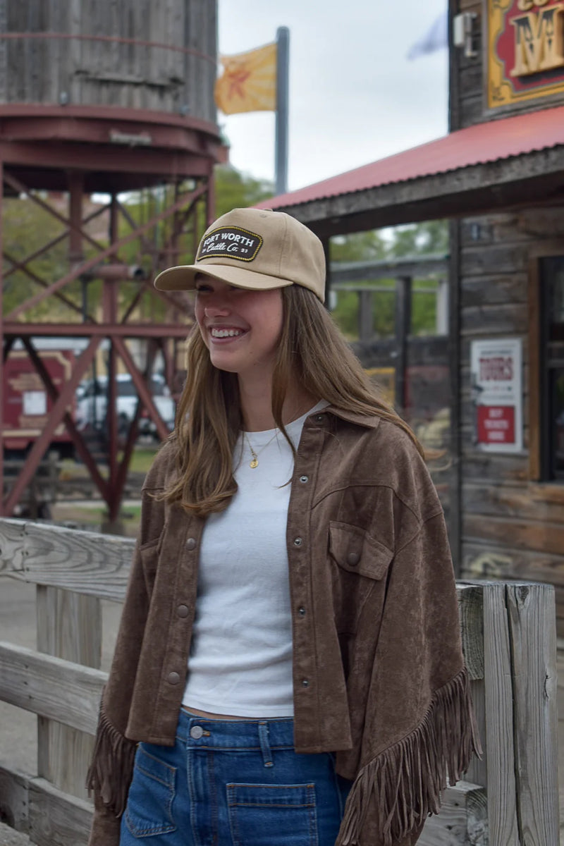 Woman wearing a cap and brown jacket standing in front of a wooden building with a sign.