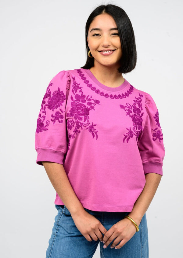 Woman wearing a pink sweatshirt with floral patterns on a plain background