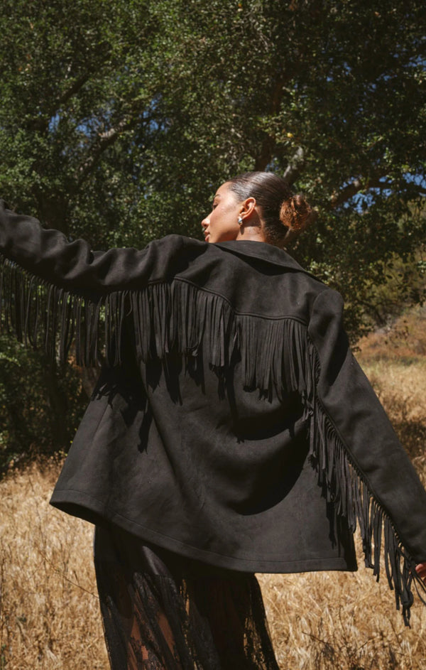 Person wearing a black fringed jacket in a natural setting