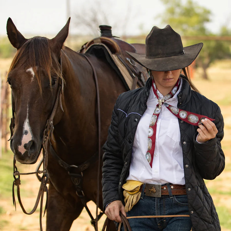 Woman in cowboy attire standing next to a horse in an outdoor setting