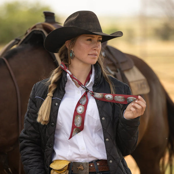 Woman in cowboy attire with a horse in the background