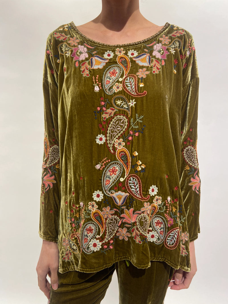 Woman wearing wide round neckline, long sleeves, and a high-low hem green velvet top with colorful embroidery