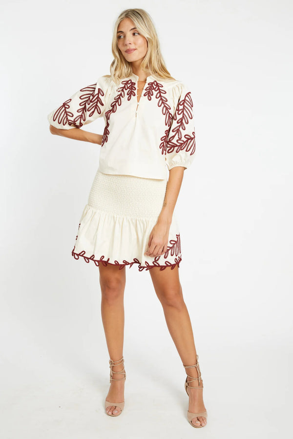 Woman wearing a white blouse with red floral embroidery and a matching skirt on a white background