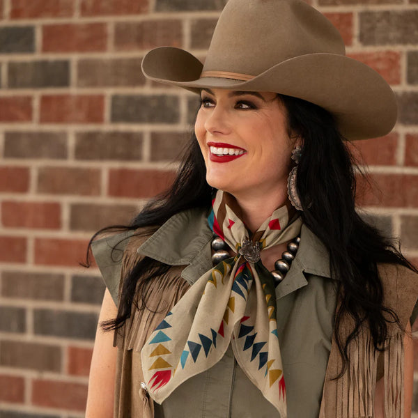 Woman wearing a cowboy hat and colorful scarf against a brick wall