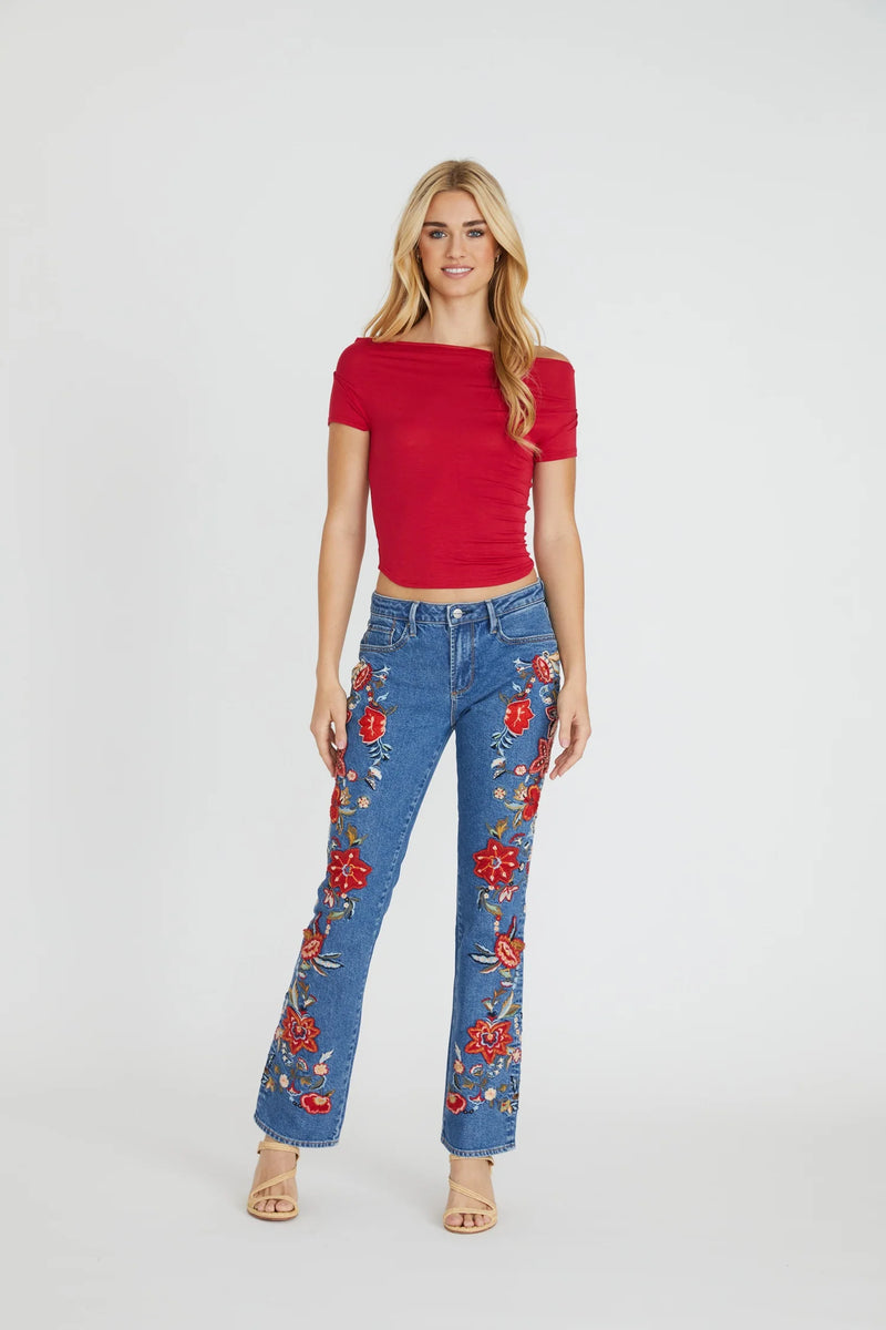 Woman wearing a red top and blue jeans with floral embroidery on a white background