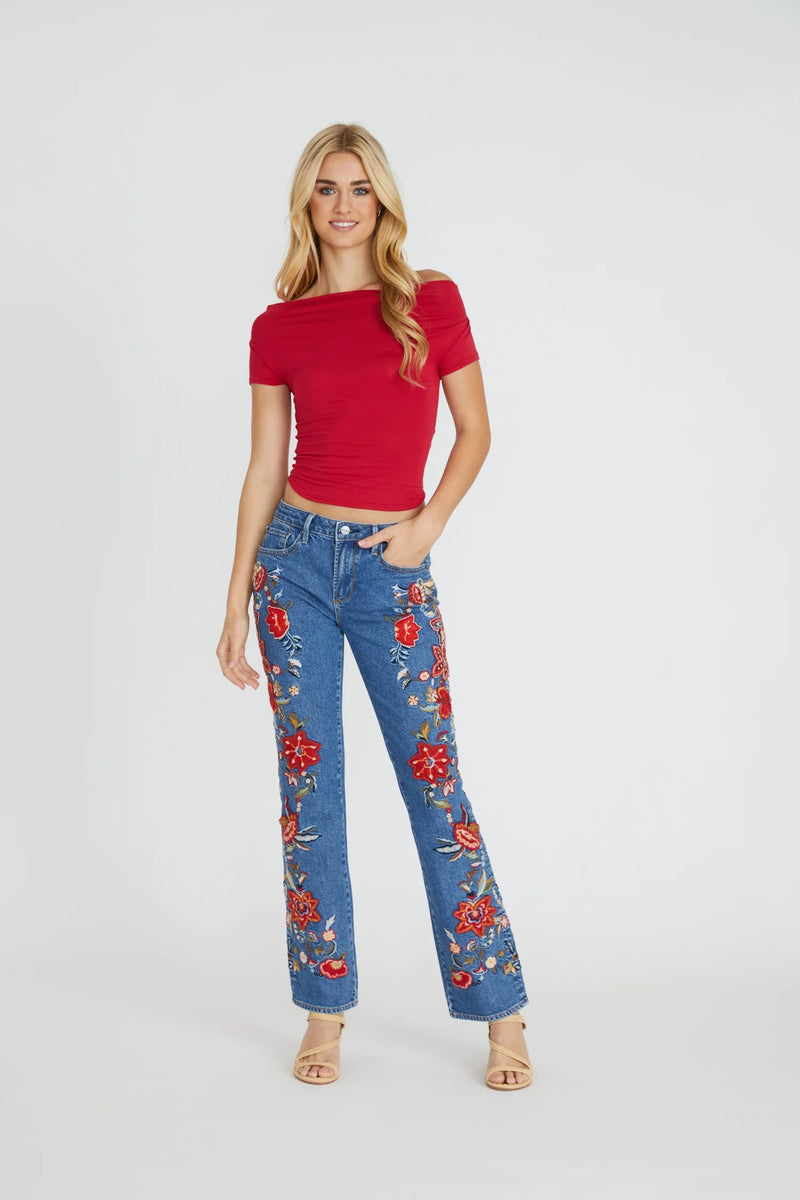 Woman wearing a red top and blue jeans with floral embroidery on a white background