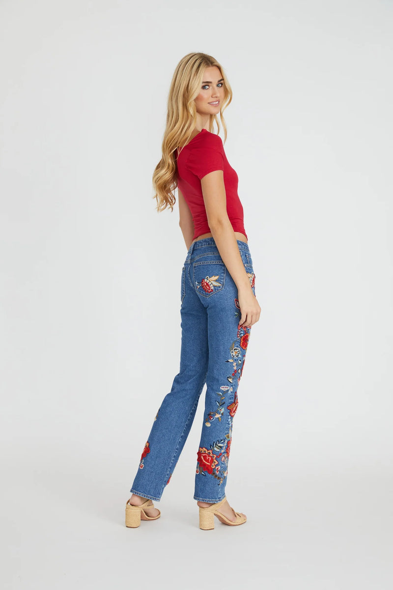 Woman wearing a red top and blue jeans with floral embroidery on a white background