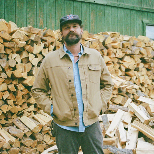 Man standing in front of wood logs wearing tan Depot Jacket with a layer of cozy jacquard flannel printed
