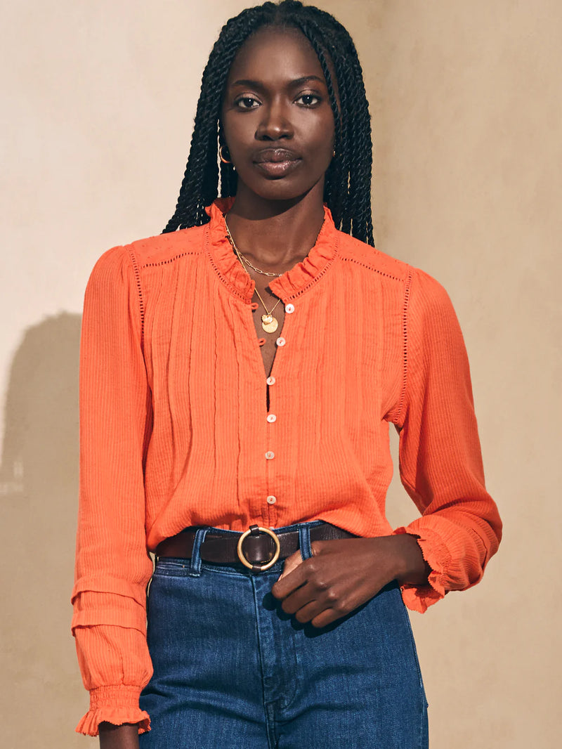 Woman wearing orange long sleeve blouse with dainty collar and buttons going down the front