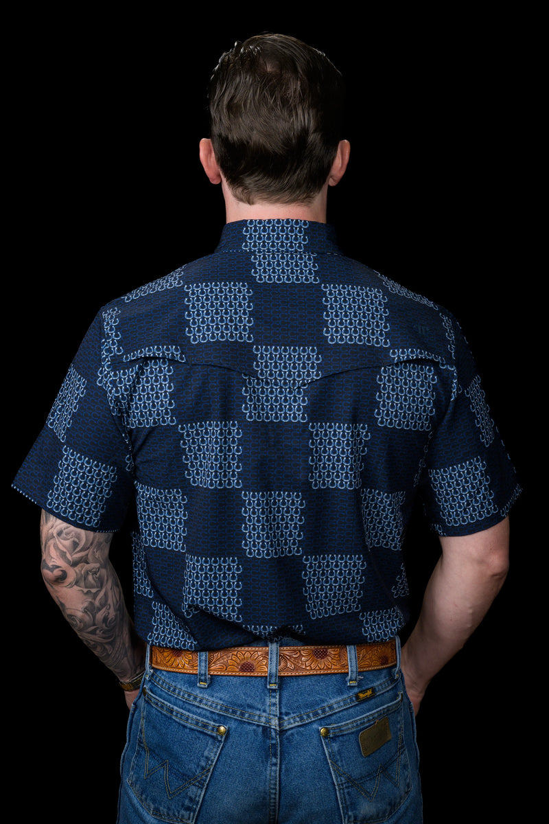Person wearing a dark blue patterned shirt and jeans on a black background