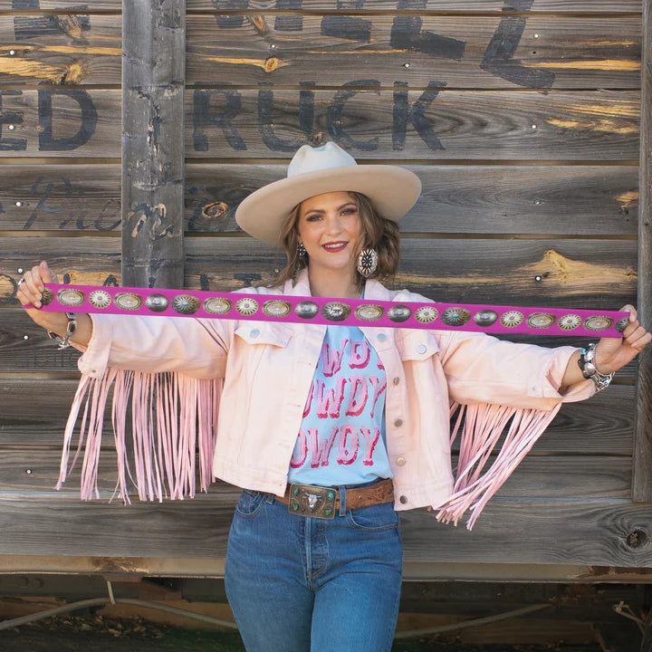 Woman holding a pink belt with fringe and conchos against a wooden background