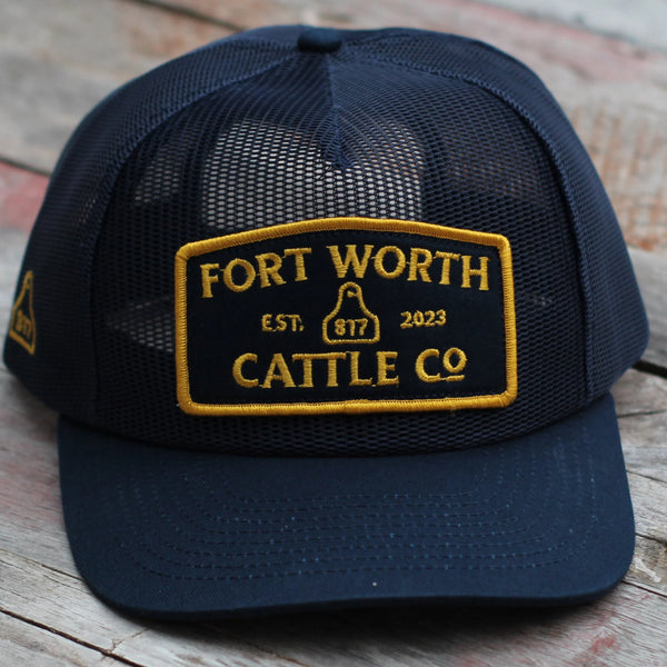 Navy blue cap with 'Fort Worth Cattle Co' logo on a wooden surface