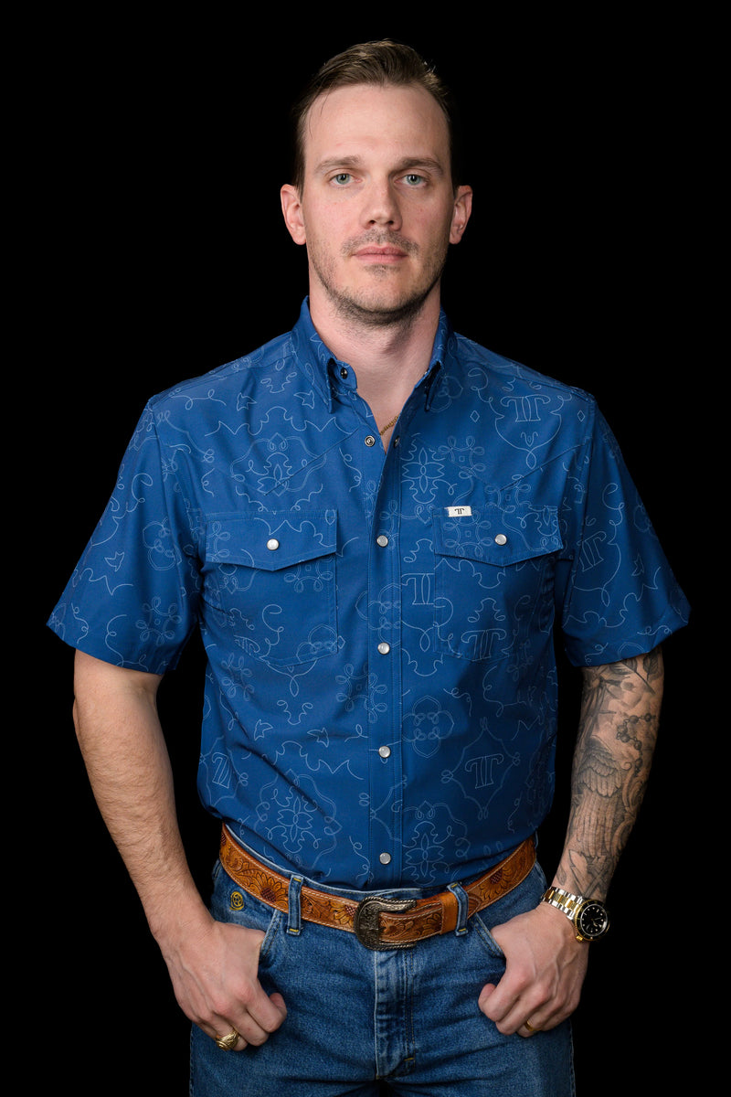 Man wearing a blue patterned shirt and jeans on a black background