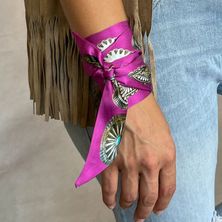 Close-up of a hand wearing a pink bracelet with silver concho details on a neutral background.