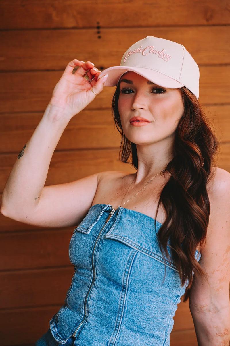 Woman wearing a beige cap and denim dress against a wooden background