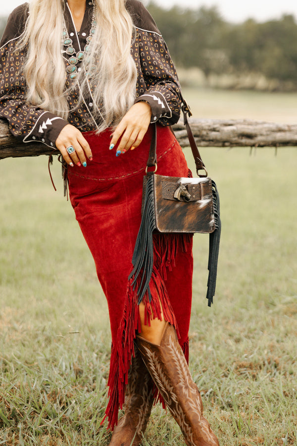 Person wearing a red skirt with fringe, brown jacket, and boots in an outdoor setting.