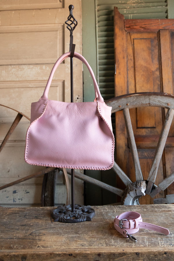 Pink handbag with matching belt on a wooden surface with rustic background