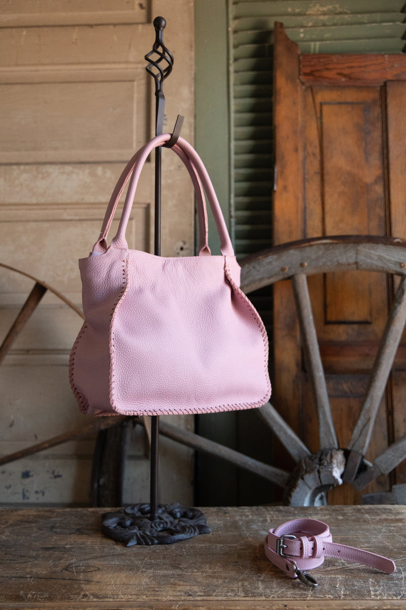 Pink handbag hanging on a hook with a wooden cart in the background