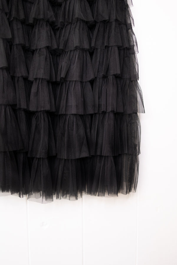 Black maxi ruffle skirt with elastic waistband on a hanger, hanging from a hook